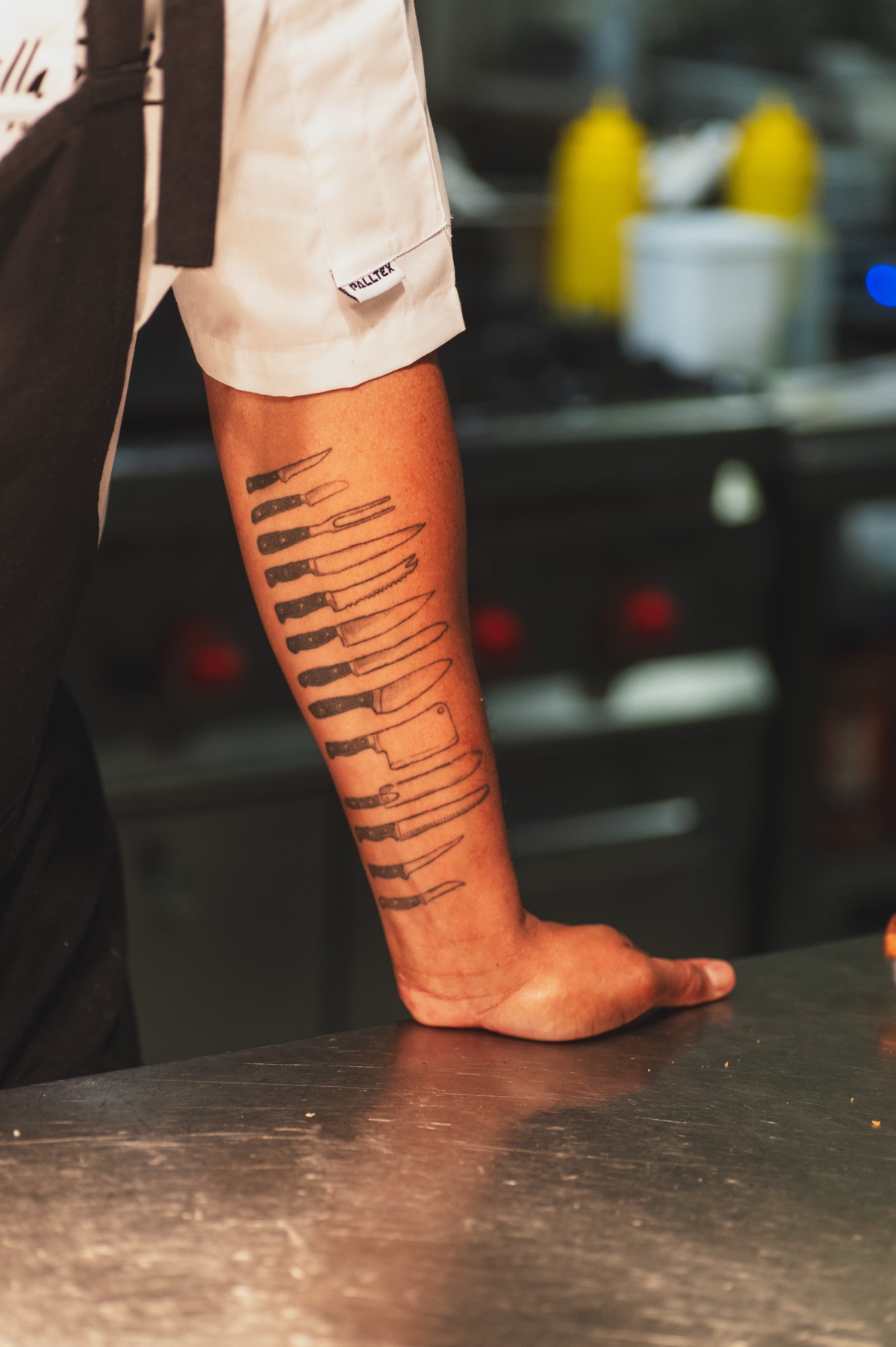 O antebraço tatuado de um chef pousado numa bancada de aço