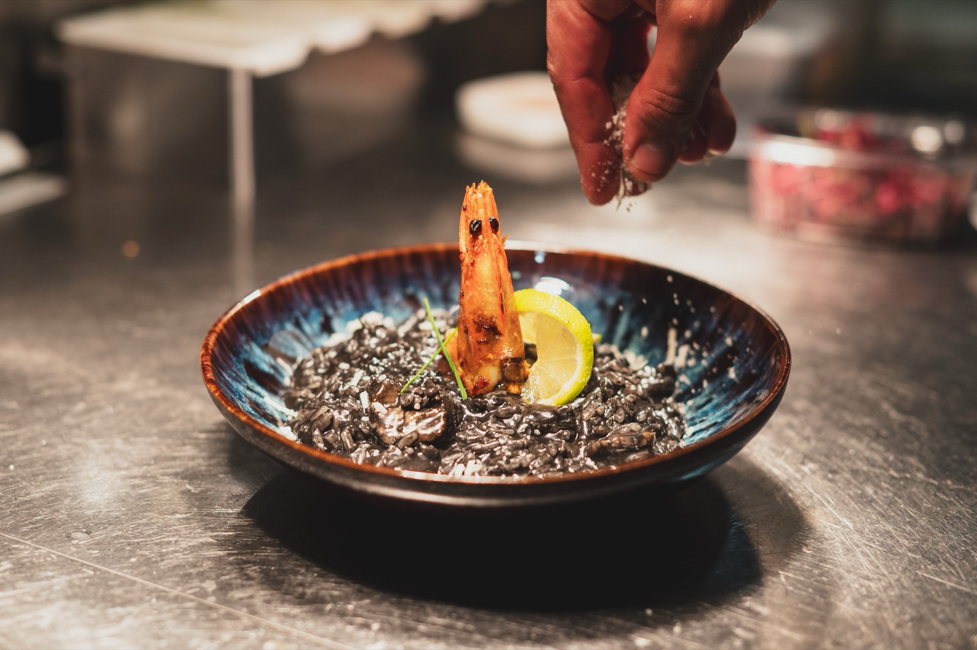 Risotto preto numa taça azul, finalizado pelas mãos do chef